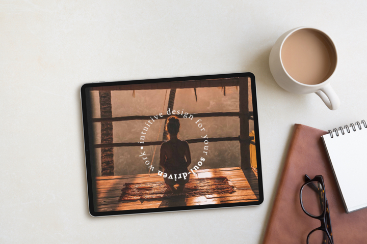 Tablet shows design layout for this webpage alongside leather-bound journal, coffee, notebook and glasses.